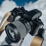 Ręce w rękawiczkach trzymają aparat Lumix z obiektywem, gotowe do uchwycenia zimowych krajobrazów.