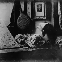 Studiowe ujęcie z początków fotografii: płaskorzeźba z postacią, dwa aniołki, pleciona butla i obrazek.