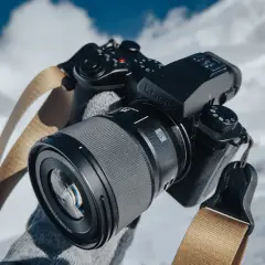 Ręce w rękawiczkach trzymają aparat Lumix z obiektywem, gotowe do uchwycenia zimowych krajobrazów.