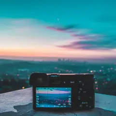 Aparat fotograficzny na tle miasta o zachodzie słońca. Na ekranie widać rozmyte światła miasta i niebo, tworzące piękne smugi światła na zdjęciach.