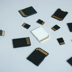 Różne rodzaje kart pamięci: microSD, SD i adaptery. Dłoń trzyma małą kartę microSD, obok leżą inne karty.