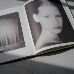 Otwarta księga z pracami Paolo Roversiego. Na lewej stronie monochromatyczny obraz tkaniny, na prawej rozmyty portret kobiety.