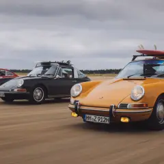 Trzy klasyczne Porsche jadące po plaży. Kompozycja dynamiczna fotografia z deskami surfingowymi na dachu.