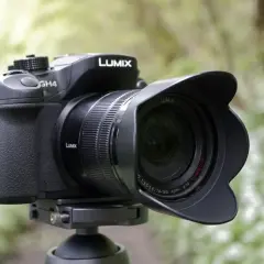 Czarny aparat Panasonic Lumix GH4 z obiektywem na statywie, w tle zielony las.