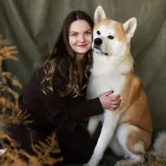 Uśmiechnięta kobieta tuli swojego psa rasy Akita. To piękne zdjecia psow, pełne ciepła i bliskości.