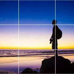 Sylwetka fotografa na plaży o zachodzie słońca, z księżycem na niebie. Kompozycja wykorzystuje trójpodział w fotografii.
