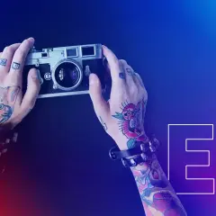 Dłonie z tatuażami trzymają aparat. To co to jest fotografia, uchwycone w kadrze z napisem EV.