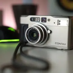 Srebrny aparat Contax TVS z obiektywem Carl Zeiss Vario-Sonnar. Obok widoczna jest czarna myszka z zielonym podświetleniem.