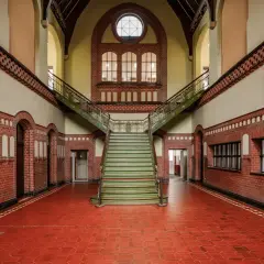 Imponująca klatka schodowa w zabytkowym budynku. Fotografia architektury z czerwonej cegły, zielonymi stopniami i ozdobnymi balustradami.