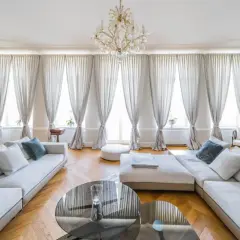 Eleganckie zdjecia wnetrz: przestronny salon z białymi sofami, kryształowym żyrandolem i zasłonami.