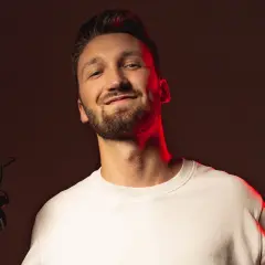 Marcin Kuciński, twórca wideo, z uśmiechem prezentuje swój sprzęt: aparat z mikrofonem i daje kciuk w górę.