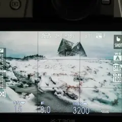 Ekran aparatu pokazuje zimowy krajobraz z opuszczonym domem. To świetny przykład, jak ustawienia wpływają na podstawy fotografii.