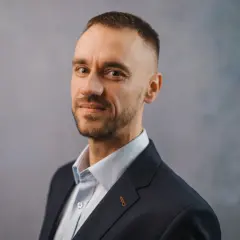 Portret Michała Wilczewskiego w ciemnej marynarce i jasnej koszuli, z lekkim zarostem i krótką fryzurą.