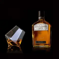 Elegancka butelka Gentleman Jack i szklanka z bursztynowym trunkiem. Stylowe zdjecia produktowe.