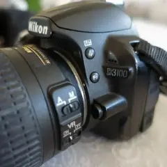 Zbliżenie na aparat Nikon D3100. Widoczne przyciski sterujące, przełącznik AF/M i VR ON/OFF. Idealny do poznawania nikon d3100 dane techniczne.