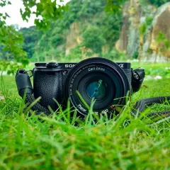 Aparat Sony z obiektywem Carl Zeiss leży na trawie. W tle skaliste wzgórza i zieleń. Idealne do fotografii przyrodniczej.