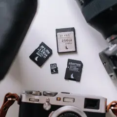 Karty pamięci SDXC i SDHC obok aparatów. Różne pojemności i adaptery.