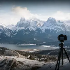 Aparat na statywie czeka na idealny kadr. Winieta fotografia górskiego krajobrazu z jeziorem i ośnieżonymi szczytami.