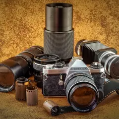 Zestaw fotograficzny: aparat Pentax JMC Super, obiektywy Vivitar i Revue, mieszek, rolki filmu. Klasyczny rodzaj aparatu fotograficznego.