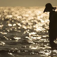 Sylwetka w kapeluszu z kołem ratunkowym na plaży. Piękna, złota bokeh fotografia falującego morza o zachodzie słońca.