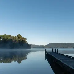 Spokojny wschód słońca nad jeziorem, mgła unosi się nad wodą, a drewniane molo zaprasza do spaceru.
