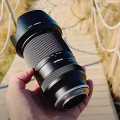 Dłoń trzyma obiektyw Tamron 28-300mm, gotowy do uchwycenia odległych detali. Jakie przybliżenie oferuje ten obiektyw?