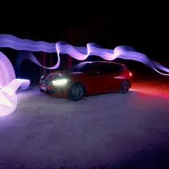 Czerwony samochód w nocnej scenerii, otoczony świetlnymi wstęgami. Ta fotografia samochodowa to magiczny taniec światła i cienia.