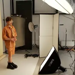 Sesja zdjęciowa w studiu. Model w pomarańczowym stroju pozuje, fotograf z aparatem sprawdza ujęcia. To właśnie jest tethering – podgląd zdjęć na żywo.