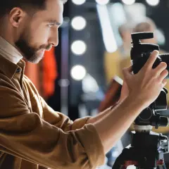 Fotograf z brodą ustawia aparat na statywie, przygotowując się do precyzyjnego pomiaru światła w studio.