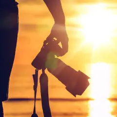 Sylwetka osoby z aparatem, gotowa do uchwycenia piękna, jak fotografować zachód słońca. Złote światło odbija się od wody.