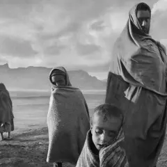 Dzieci i dorosły owinięci w tkaniny, w surowym krajobrazie. Wzrok przyciąga spojrzenie jednego z nich, uchwycone przez Sebastiao Salgado.