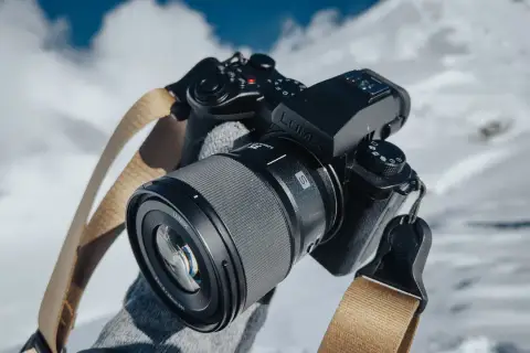 Ręce w rękawiczkach trzymają aparat Lumix z obiektywem, gotowe do uchwycenia zimowych krajobrazów.