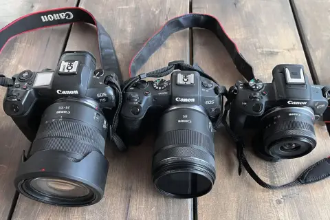 Trzy aparaty Canon EOS: R5 z obiektywem 24-105mm, RP z 85mm i R50 z 18-45mm. Różne obiektywy, od szerokokątnych po tele, pokazują wszechstronność systemu.