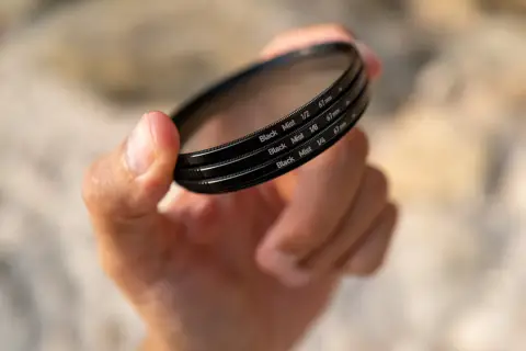 Dłoń trzyma filtr fotograficzny z napisem "Black Mist", który nadaje zdjęciom subtelny, mglisty efekt.