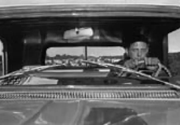 Lee Friedlander za kierownicą, patrzący przed siebie. Widok z wnętrza samochodu.