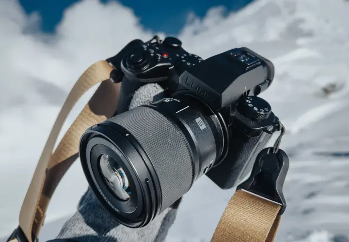 Ręce w rękawiczkach trzymają aparat Lumix z obiektywem, gotowe do uchwycenia zimowych krajobrazów.