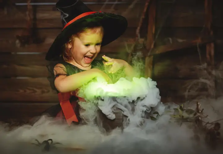 Mała czarownica w kapeluszu miesza w kociołku, tworząc zielony dym. To jak zrobic dym na Halloween!