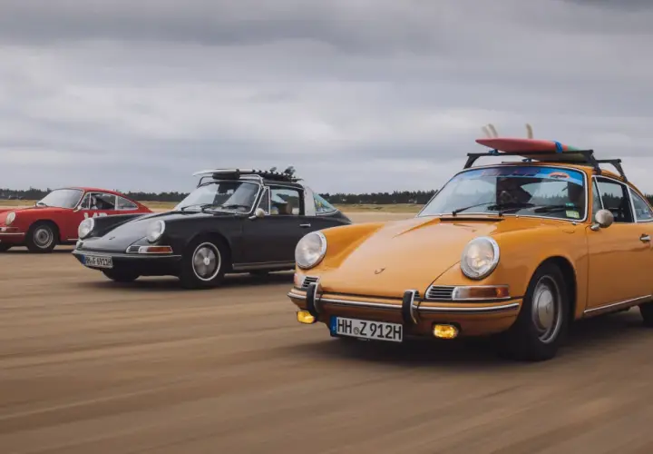 Trzy klasyczne Porsche jadące po plaży. Kompozycja dynamiczna fotografia z deskami surfingowymi na dachu.
