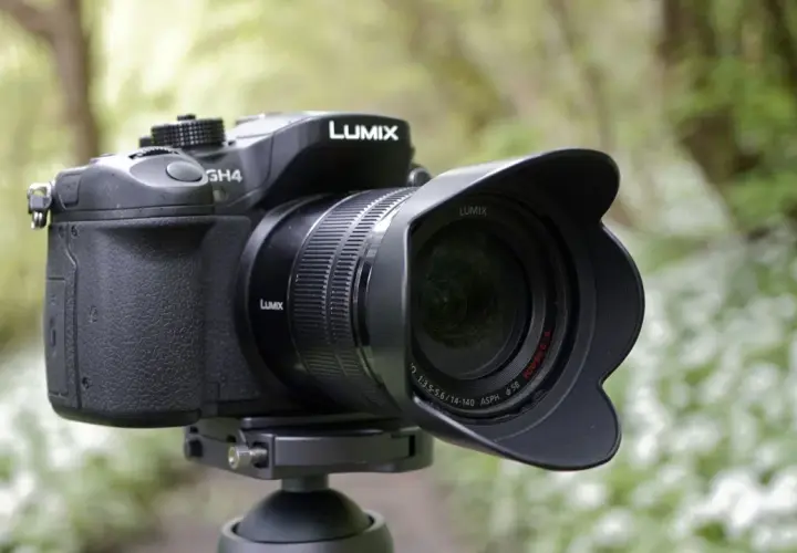 Czarny aparat Panasonic Lumix GH4 z obiektywem na statywie, w tle zielony las.
