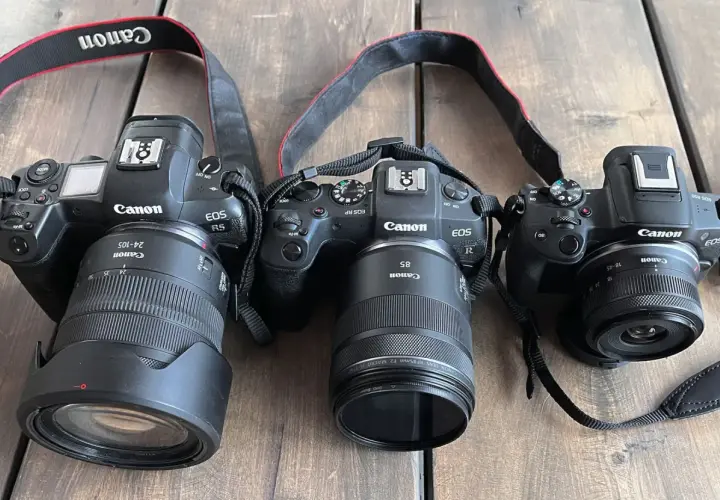 Trzy aparaty Canon EOS: R5 z obiektywem 24-105mm, RP z 85mm i R50 z 18-45mm. Różne obiektywy, od szerokokątnych po tele, pokazują wszechstronność systemu.