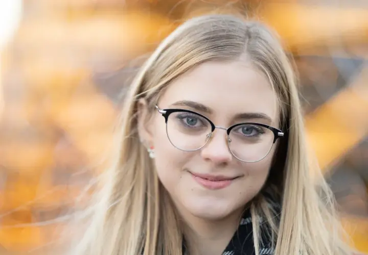 Uśmiechnięta blondynka w okularach, z rozmyciem tła. Idealna ogniskowa do portretu, by podkreślić oczy.