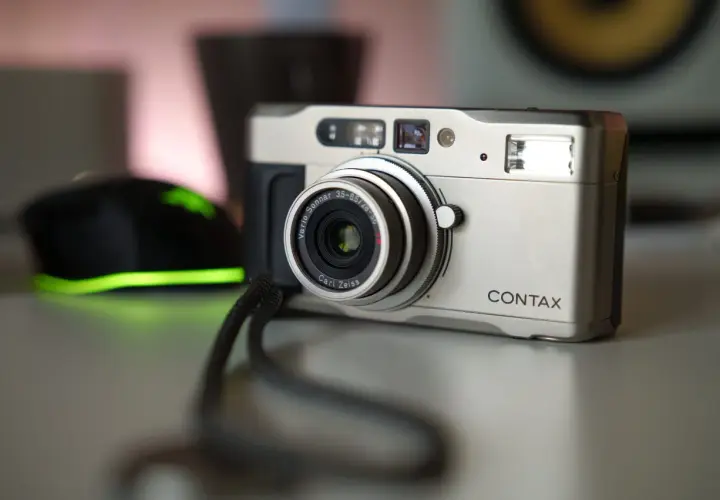Srebrny aparat Contax TVS z obiektywem Carl Zeiss Vario-Sonnar. Obok widoczna jest czarna myszka z zielonym podświetleniem.