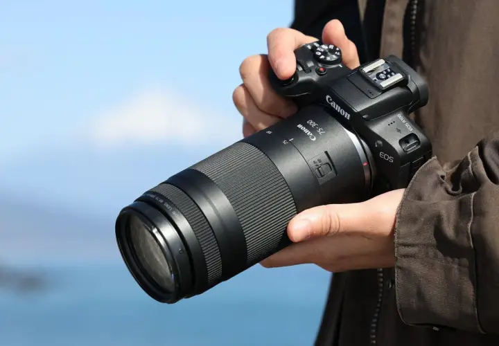 Dłoń trzyma aparat Canon z obiektywem 75-300, idealnym do fotografii przyrodniczej i sportowej, pozwalającym uchwycić odległe detale.