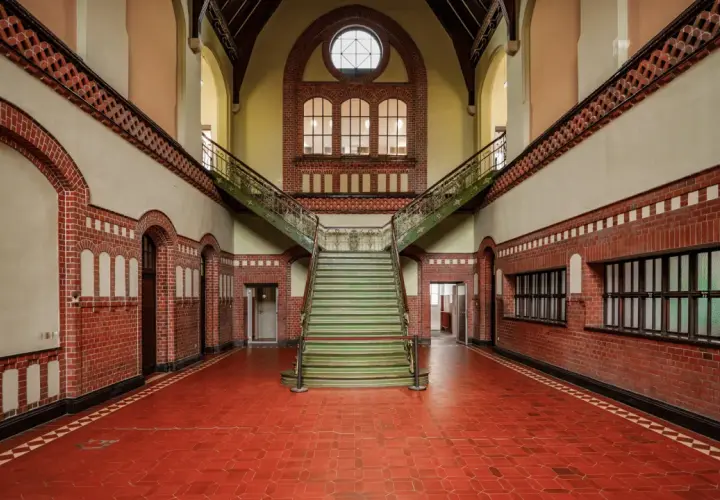 Imponująca klatka schodowa w zabytkowym budynku. Fotografia architektury z czerwonej cegły, zielonymi stopniami i ozdobnymi balustradami.