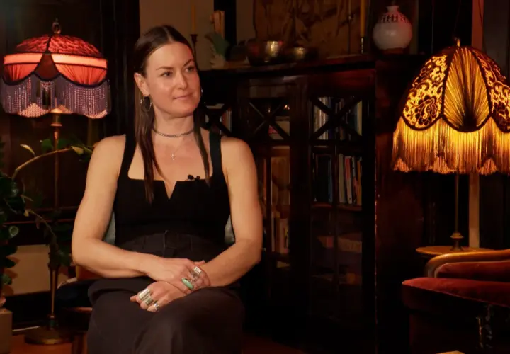 Magdalena Wosińska w stylowym wnętrzu, siedzi obok lampy z frędzlami.