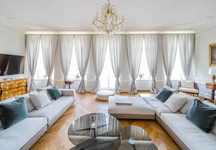 Eleganckie zdjecia wnetrz: przestronny salon z białymi sofami, kryształowym żyrandolem i zasłonami.