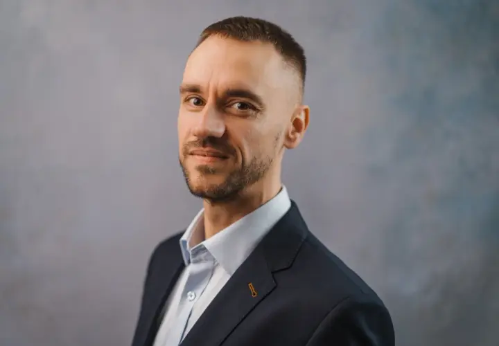 Portret Michała Wilczewskiego w ciemnej marynarce i jasnej koszuli, z lekkim zarostem i krótką fryzurą.