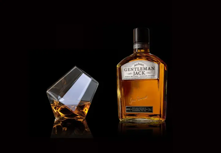 Elegancka butelka Gentleman Jack i szklanka z bursztynowym trunkiem. Stylowe zdjecia produktowe.