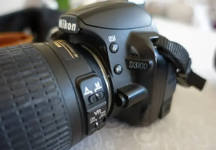 Zbliżenie na aparat Nikon D3100. Widoczne przyciski sterujące, przełącznik AF/M i VR ON/OFF. Idealny do poznawania nikon d3100 dane techniczne.