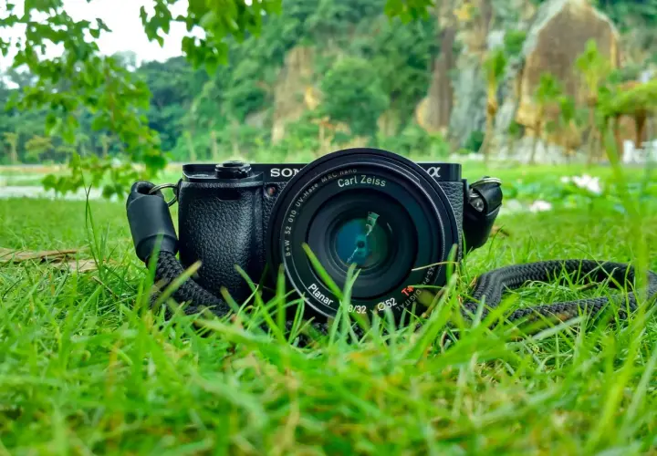 Aparat Sony z obiektywem Carl Zeiss leży na trawie. W tle skaliste wzgórza i zieleń. Idealne do fotografii przyrodniczej.
